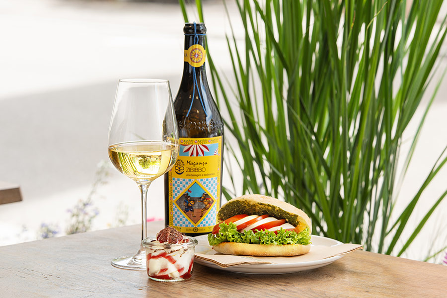 Glas Sommerwein mit Panino und Dessert im Glas sowie einer Flasche Wein auf einem Tisch arrangiert